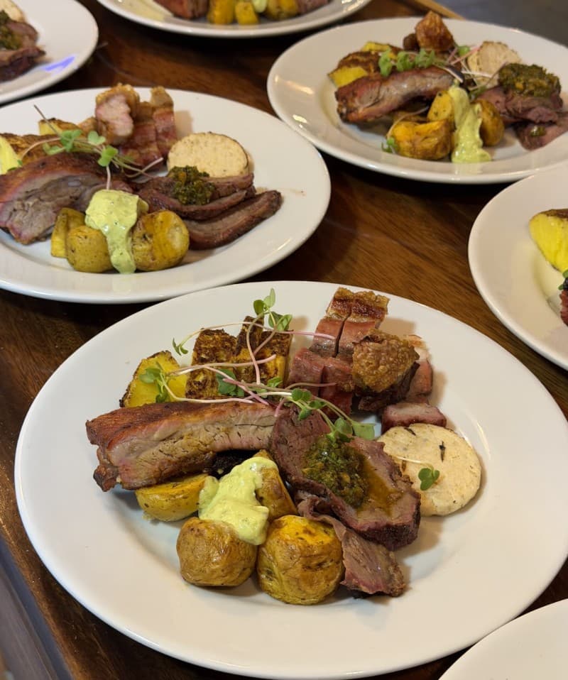 Platos del asado al barril con carnes, papa criolla, arepa y chimichurri