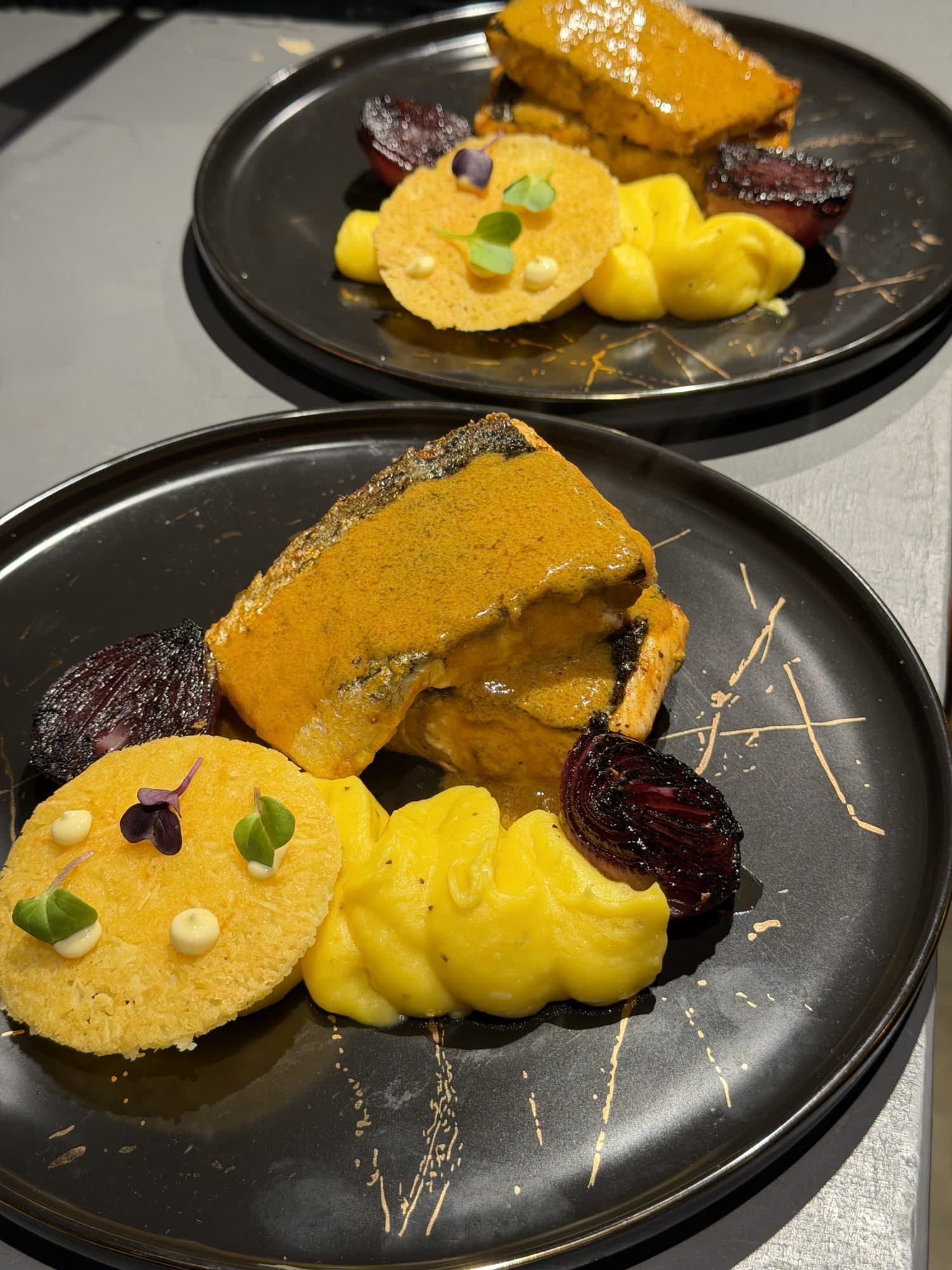Pescado en salsa con cebolla asada, servido en plato negro