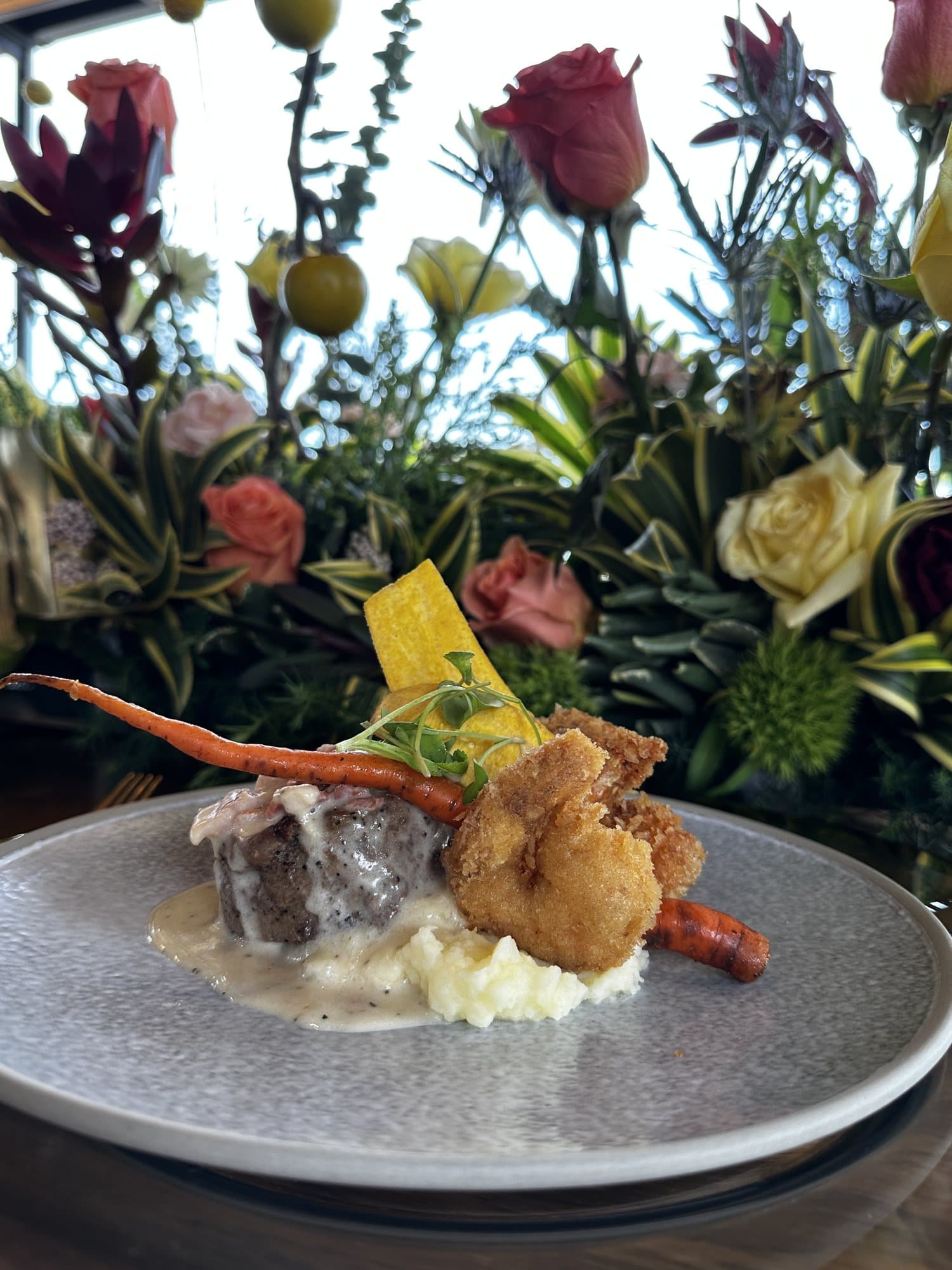 Plato fuerte con puré y zanahoria asada, entre flores